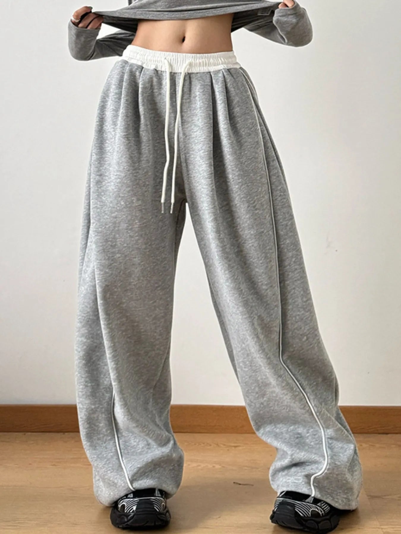 Person wearing gray sweatpants with a white waistband on a plain background