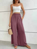 Woman wearing a white top and purple wide-leg pants against a plain background