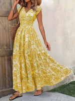 Woman wearing a yellow floral dress standing against a wooden wall.
