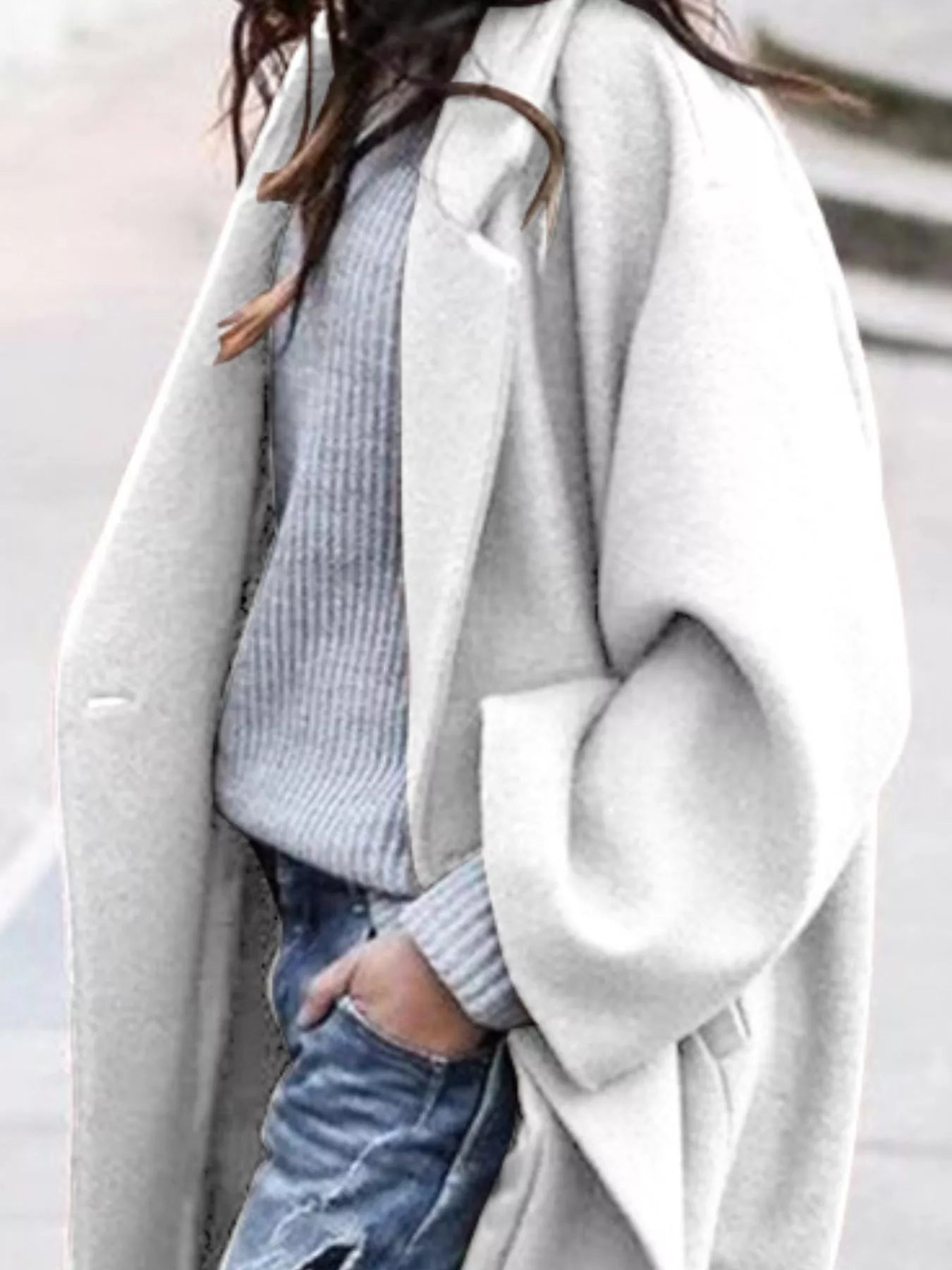 Person wearing a light gray coat over a blue sweater and jeans on a neutral background