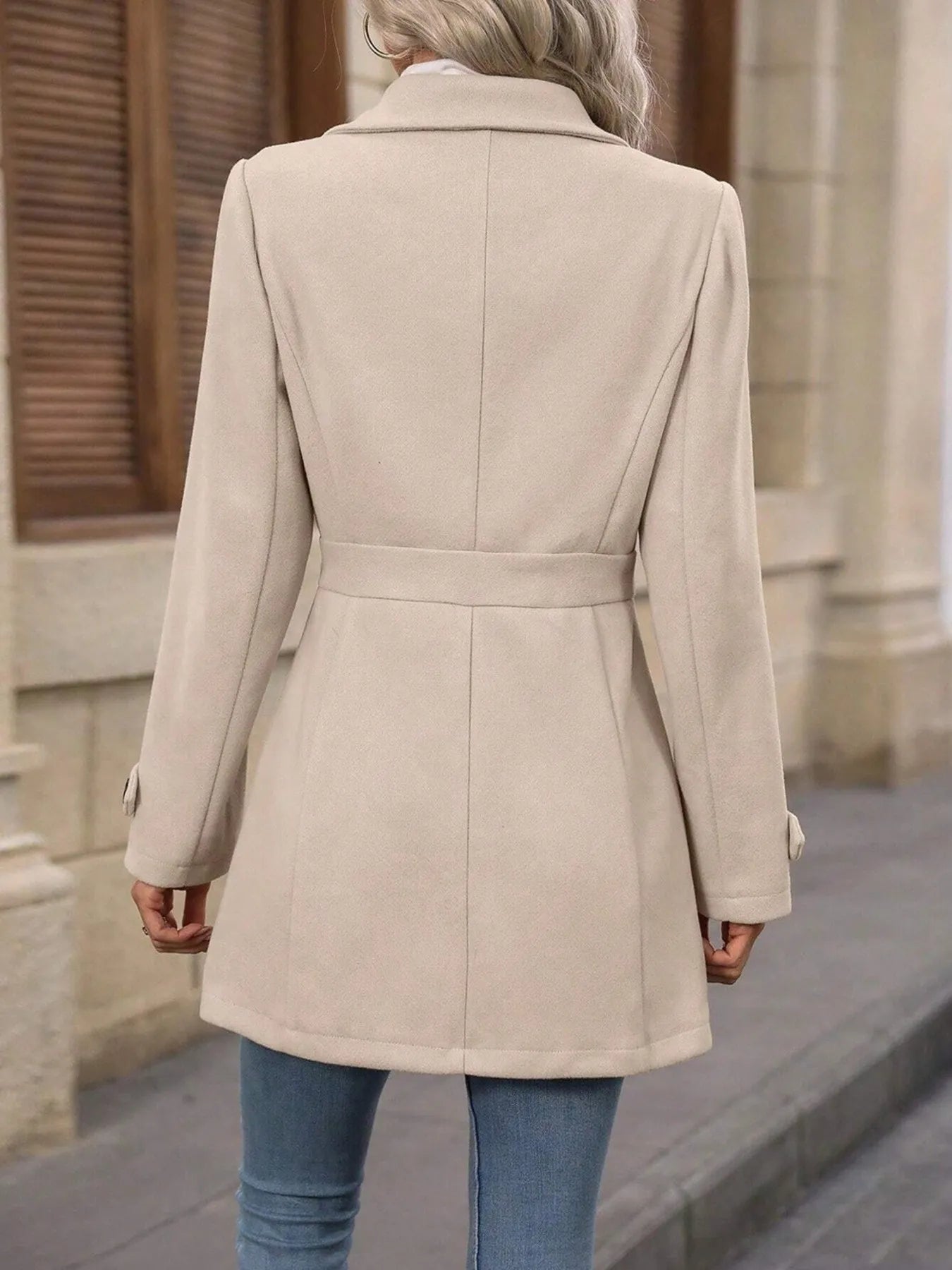 Person wearing a beige coat walking outdoors on a sidewalk.