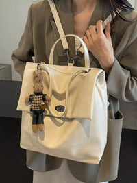 Beige handbag with a teddy bear keychain held by a person wearing a beige coat.
