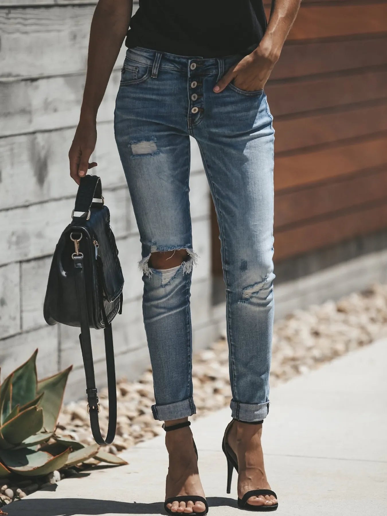 Person wearing ripped blue jeans holding a black bag outdoors.