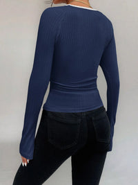 Person wearing a blue ribbed long-sleeve top and black pants on a plain background