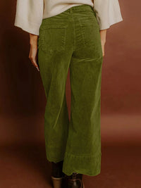 Green corduroy pants worn by a person on a brown background