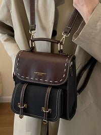 Brown and black leather handbag with visible brand name, worn by a person in a beige coat.