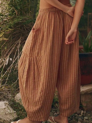 Person wearing brown striped pants standing outdoors with plants in the background