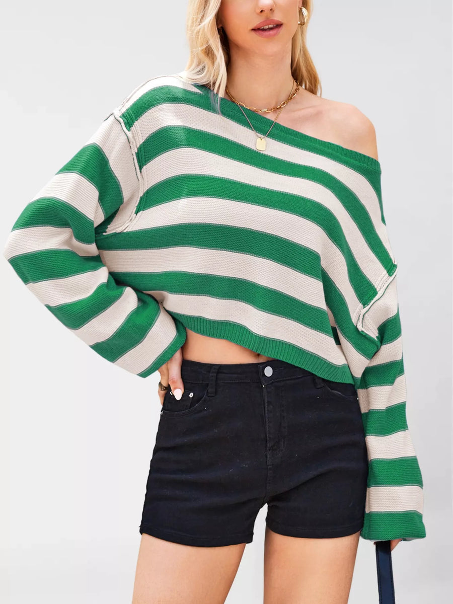 Person wearing a green and white striped sweater with black shorts on a plain background