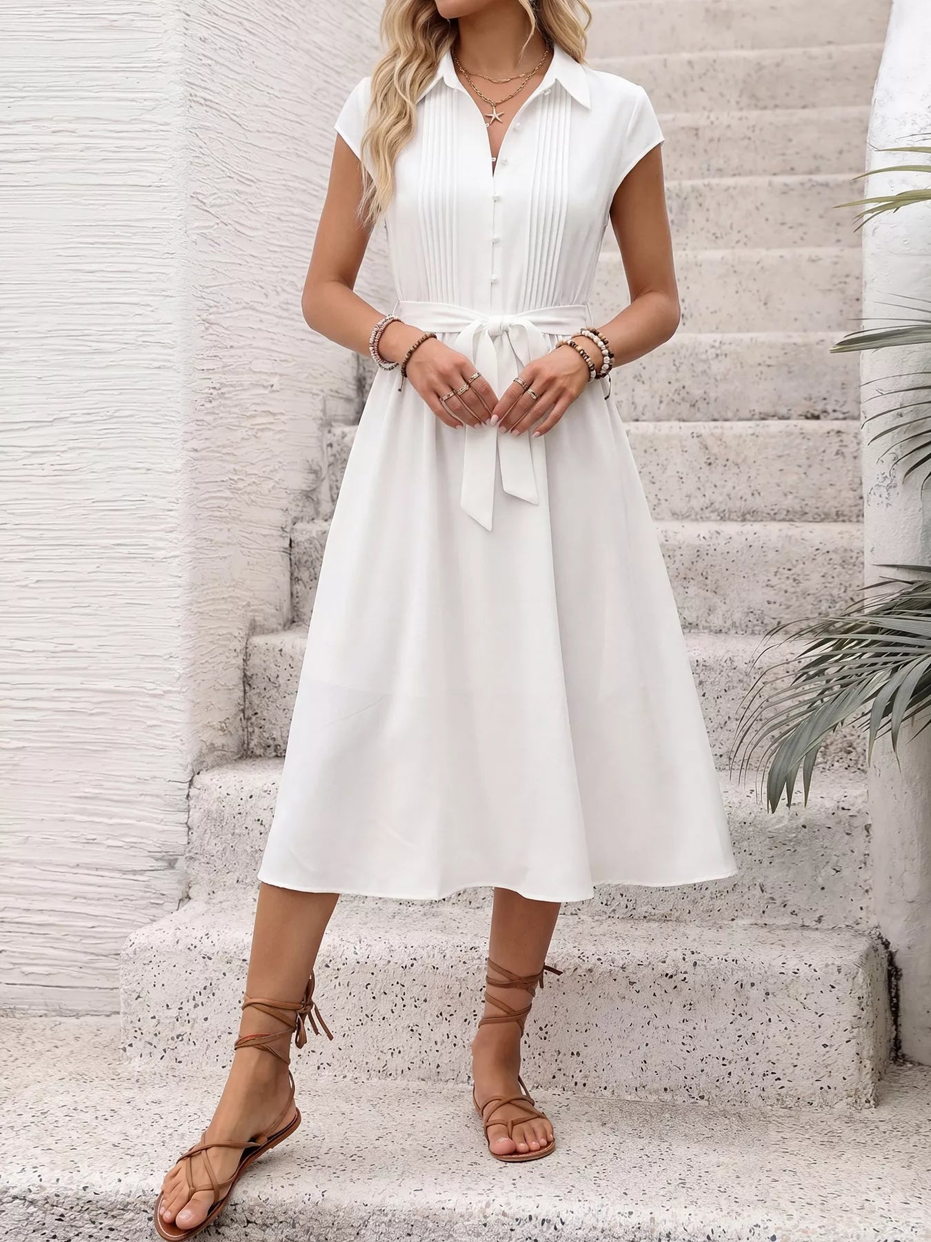 Woman wearing a white dress standing on stone steps with a neutral background