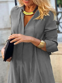 Woman wearing a gray dress with a yellow necklace and gold bracelet, holding a black clutch.