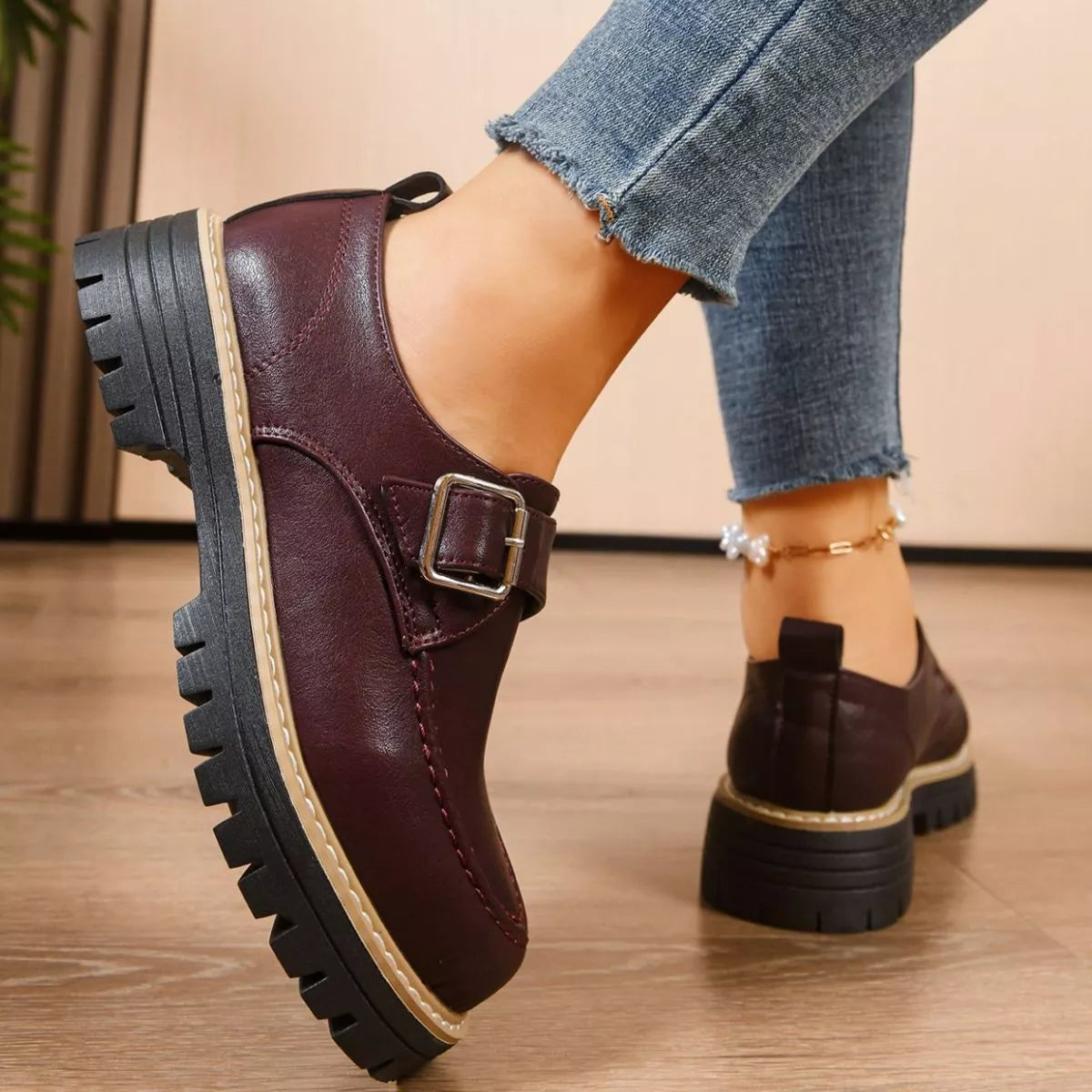 Brown leather shoes with a buckle worn by a person on a wooden floor.