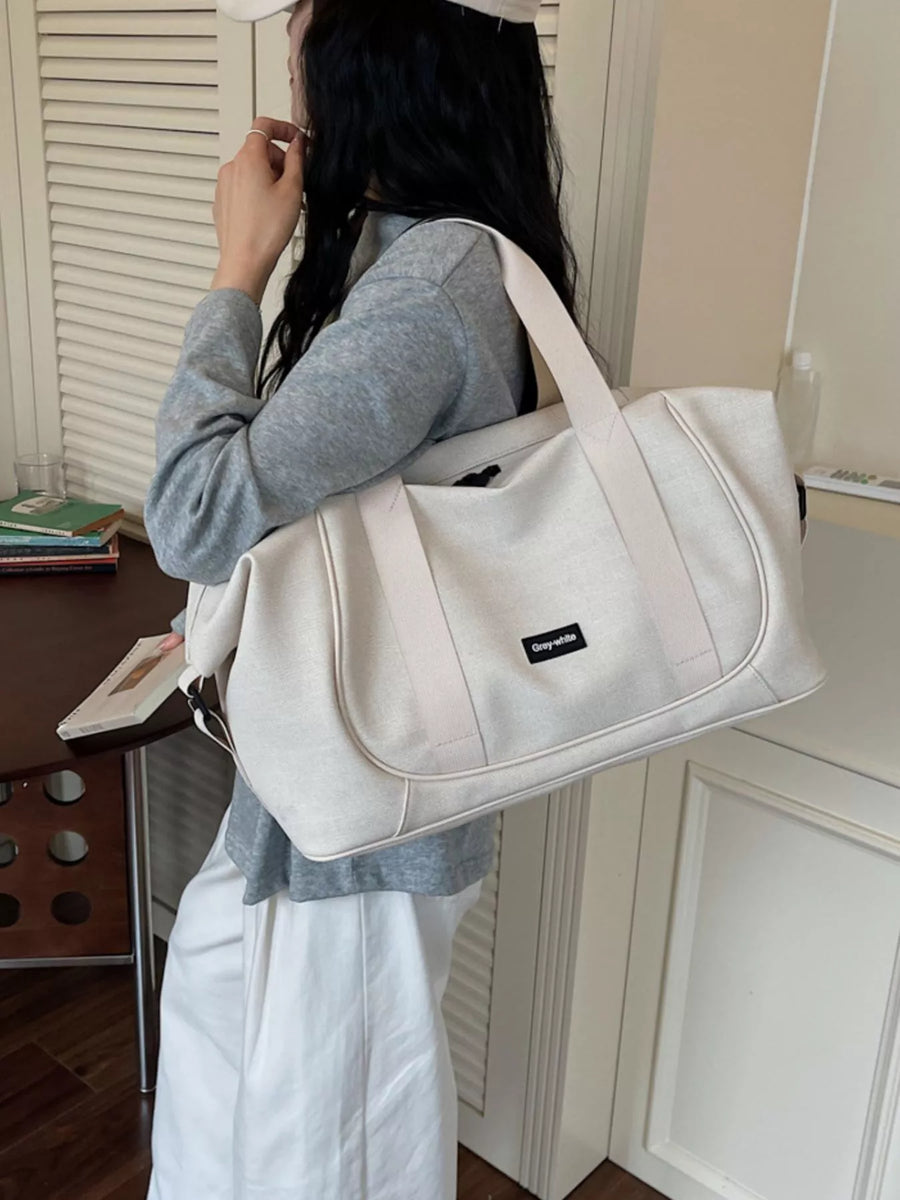 Person holding a white duffel bag with a visible brand logo in an indoor setting.