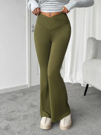 Person wearing olive green flared pants in a room with a white wall and gray carpet.