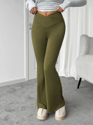 Person wearing olive green flared pants in a room with a white wall and gray carpet.
