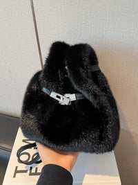 Black fur bag held by a hand with a neutral background