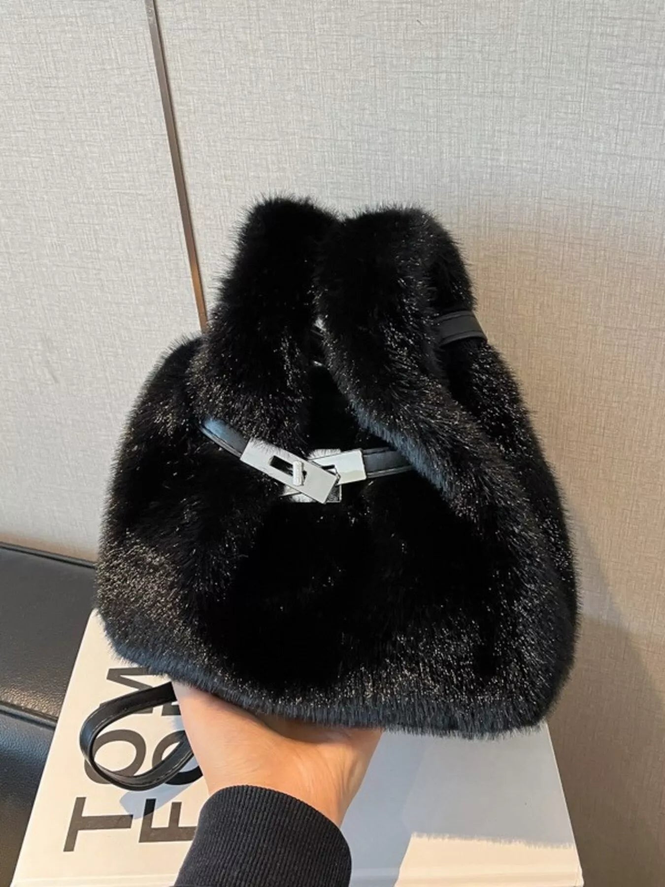 Black fur bag held by a hand with a neutral background