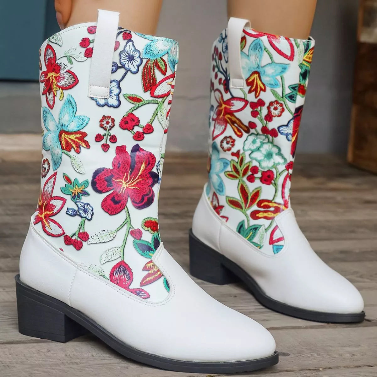 White boots with colorful floral embroidery on a wooden floor.