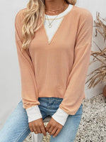 Person wearing a ribbed pink sweater with white trim, sitting on a stone surface.