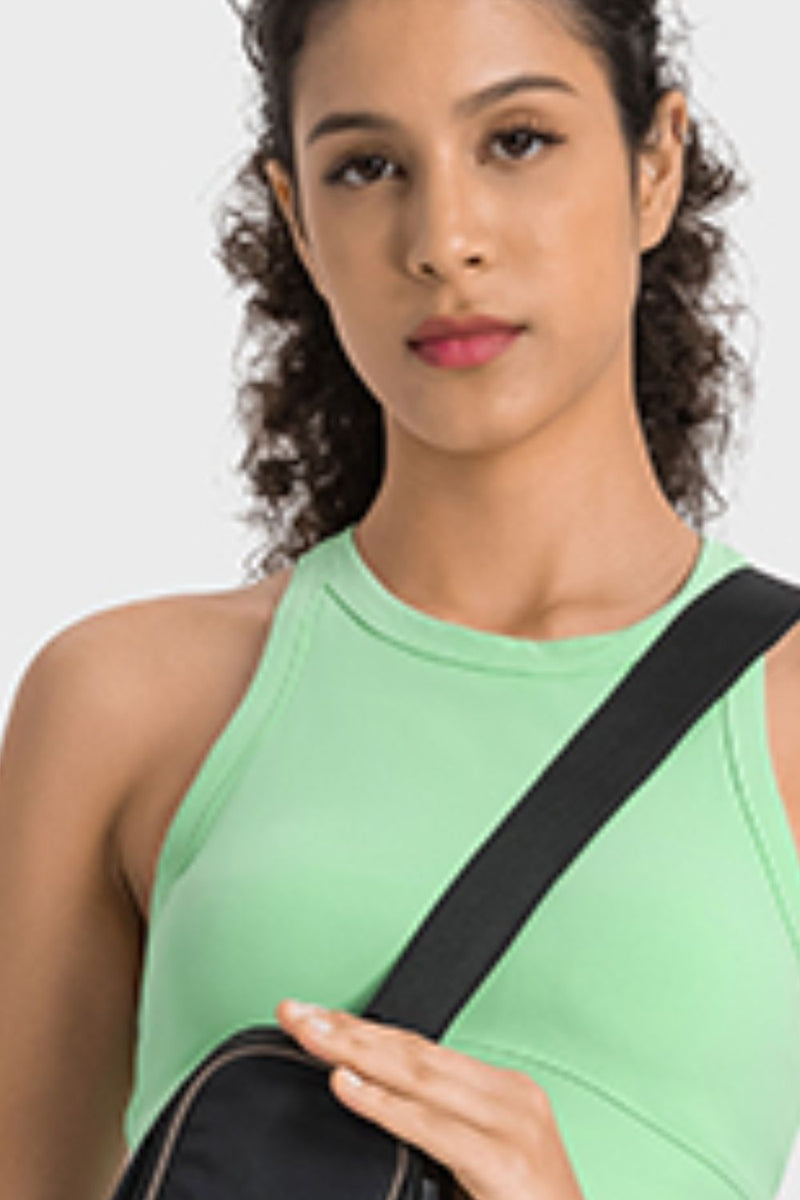 Woman wearing a green sleeveless top with a black strap over her shoulder on a white background