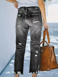 Person wearing black distressed jeans holding a brown handbag on a light blue background