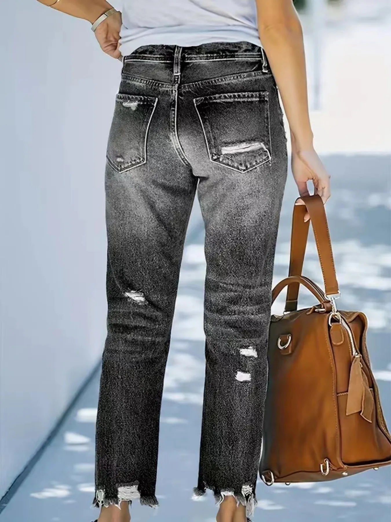 Person wearing black distressed jeans holding a brown handbag on a light blue background