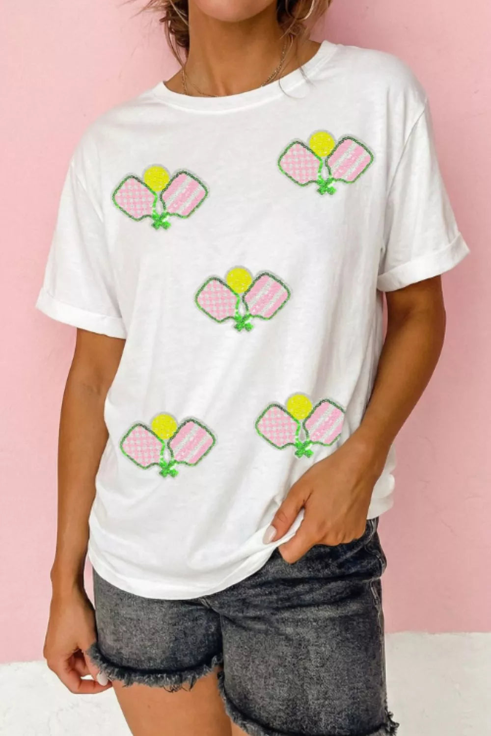 Person wearing a white t-shirt with tennis racket designs on a pink background