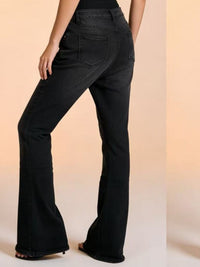 Black flared jeans worn by a person on a beige background