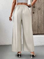 Person wearing beige wide-leg pants with a white top and high heels, standing against a wooden door.