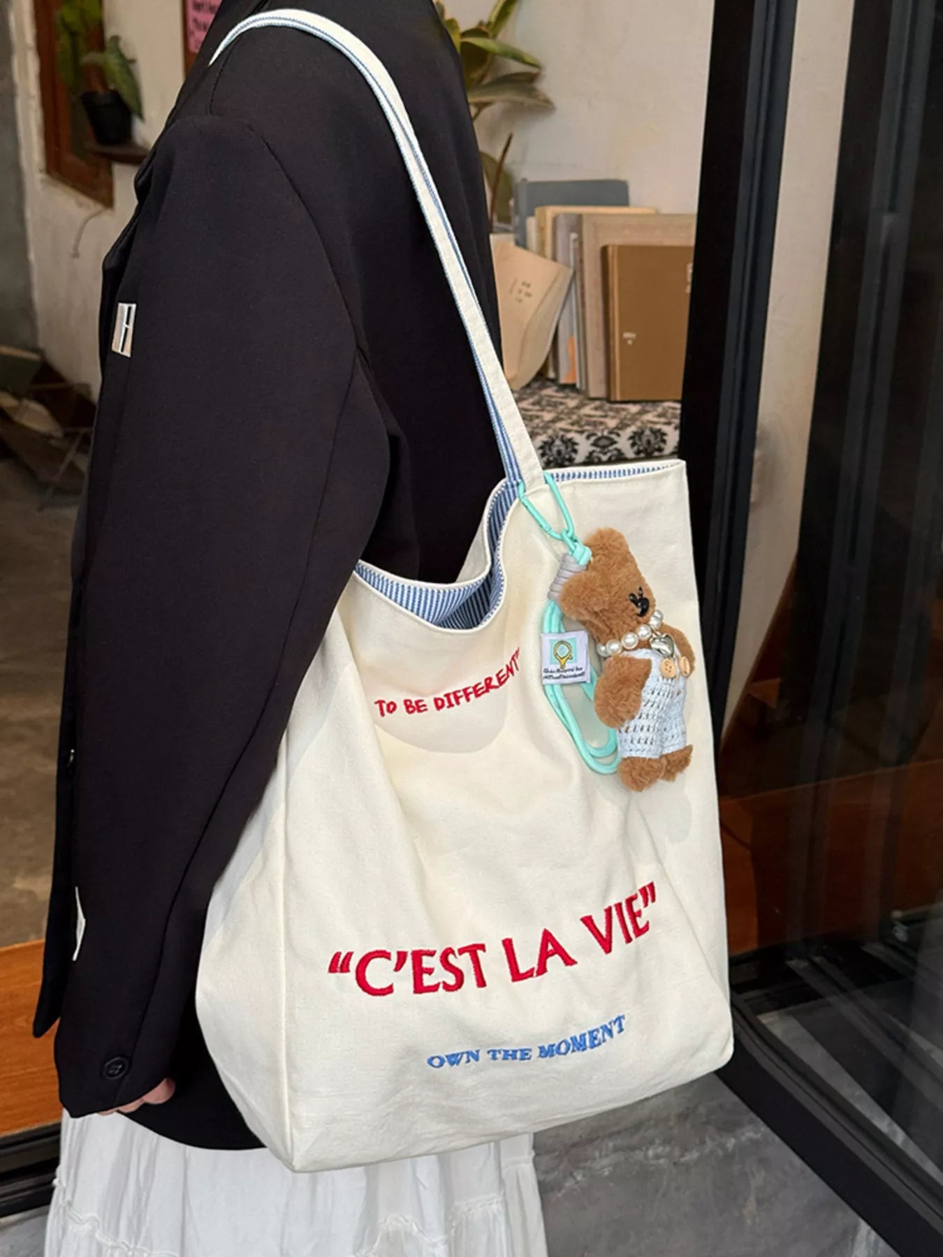 Person holding a tote bag with a teddy bear and text, standing indoors.
