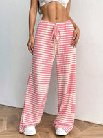 Person wearing pink and white checkered pants with a white top on a plain background