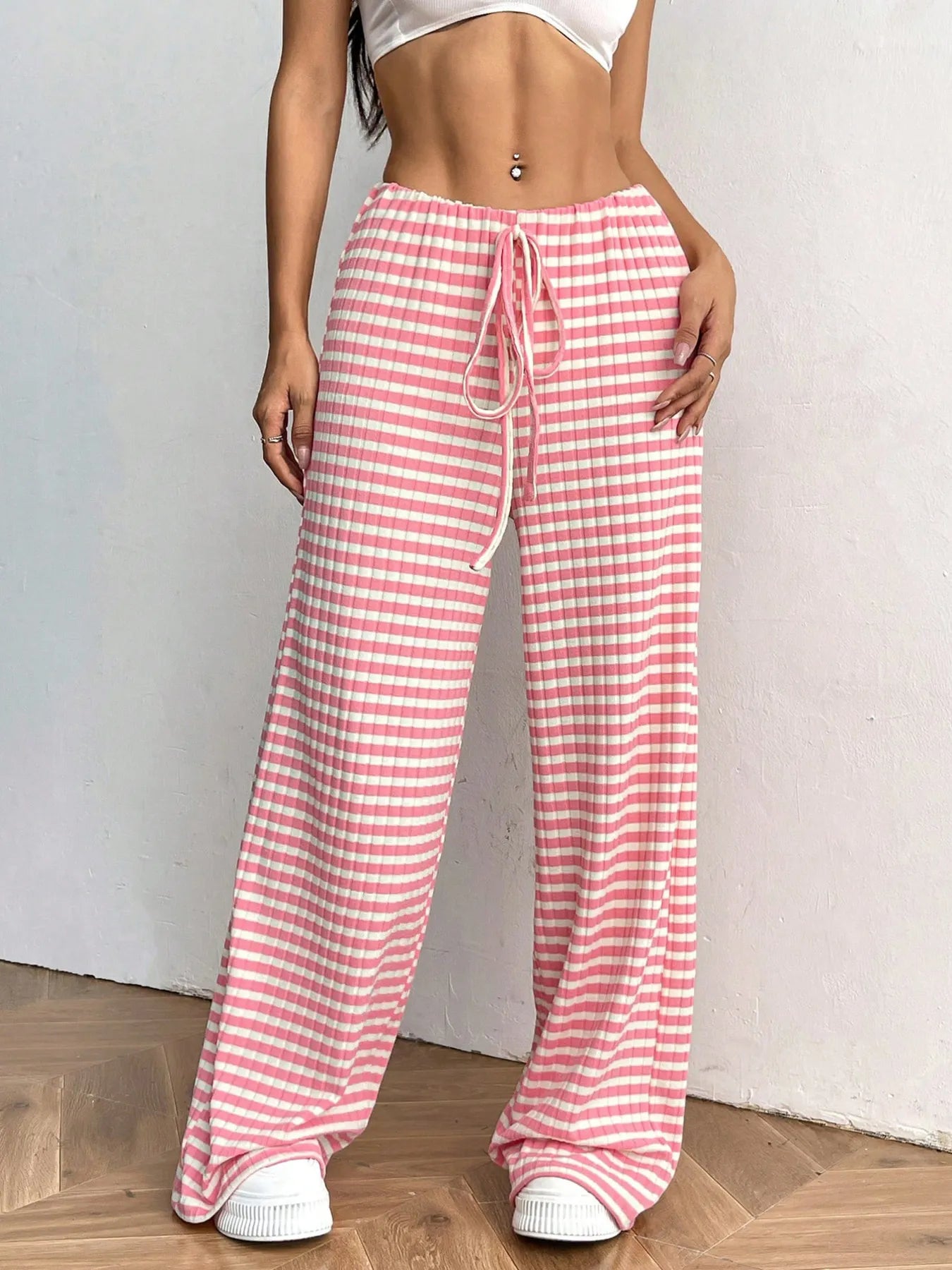 Person wearing pink and white checkered pants with a white top on a plain background