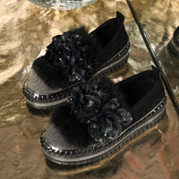 Black platform shoes with floral embellishments on a reflective gold surface