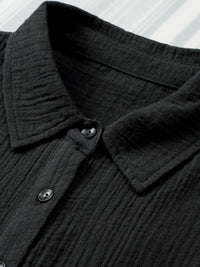 Close-up of a black textured shirt collar with buttons on a white background