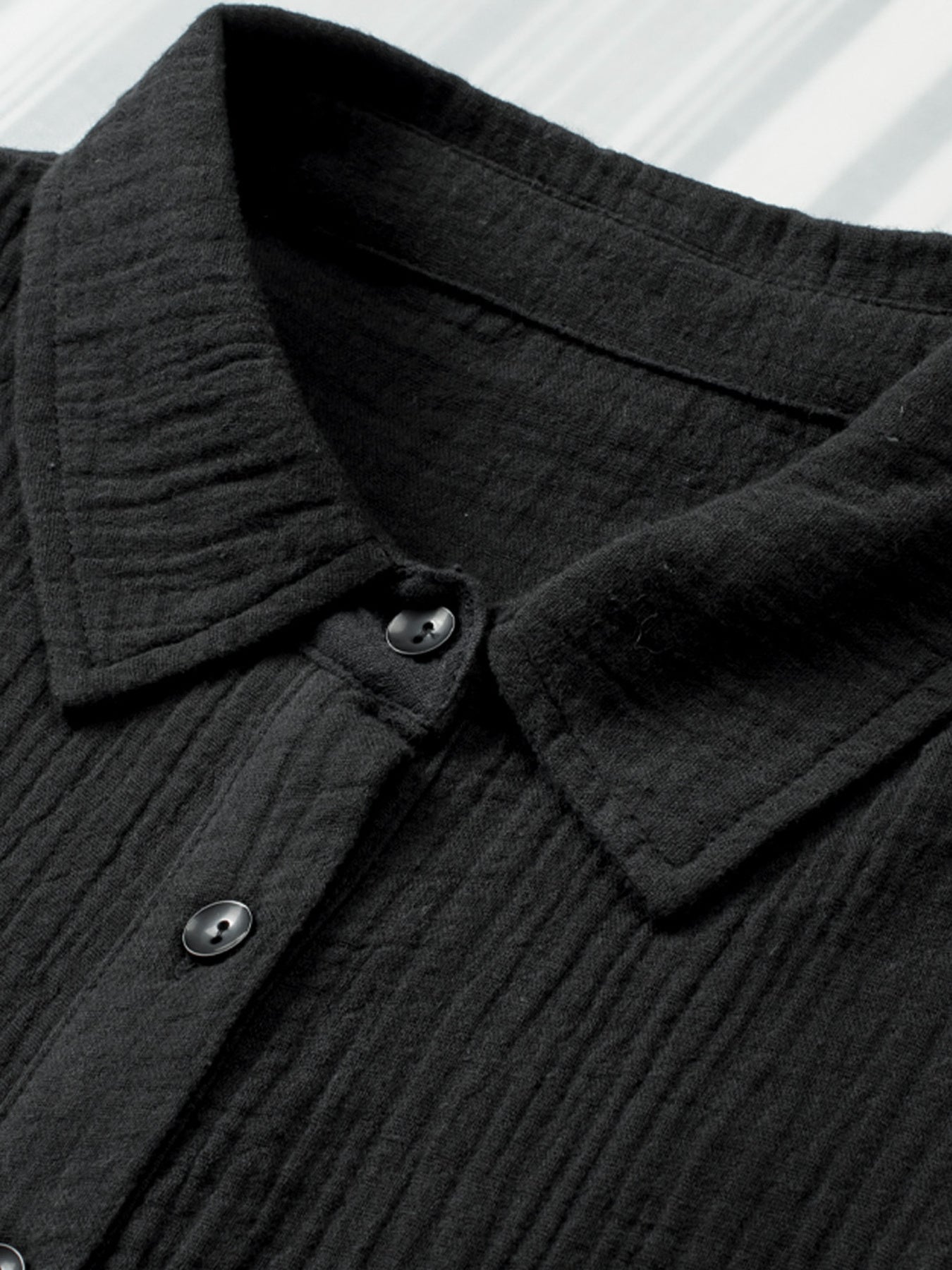 Close-up of a black textured shirt collar with buttons on a white background
