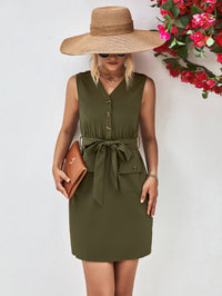 Woman wearing an olive green dress with a wide-brimmed hat and holding a clutch against a white background.