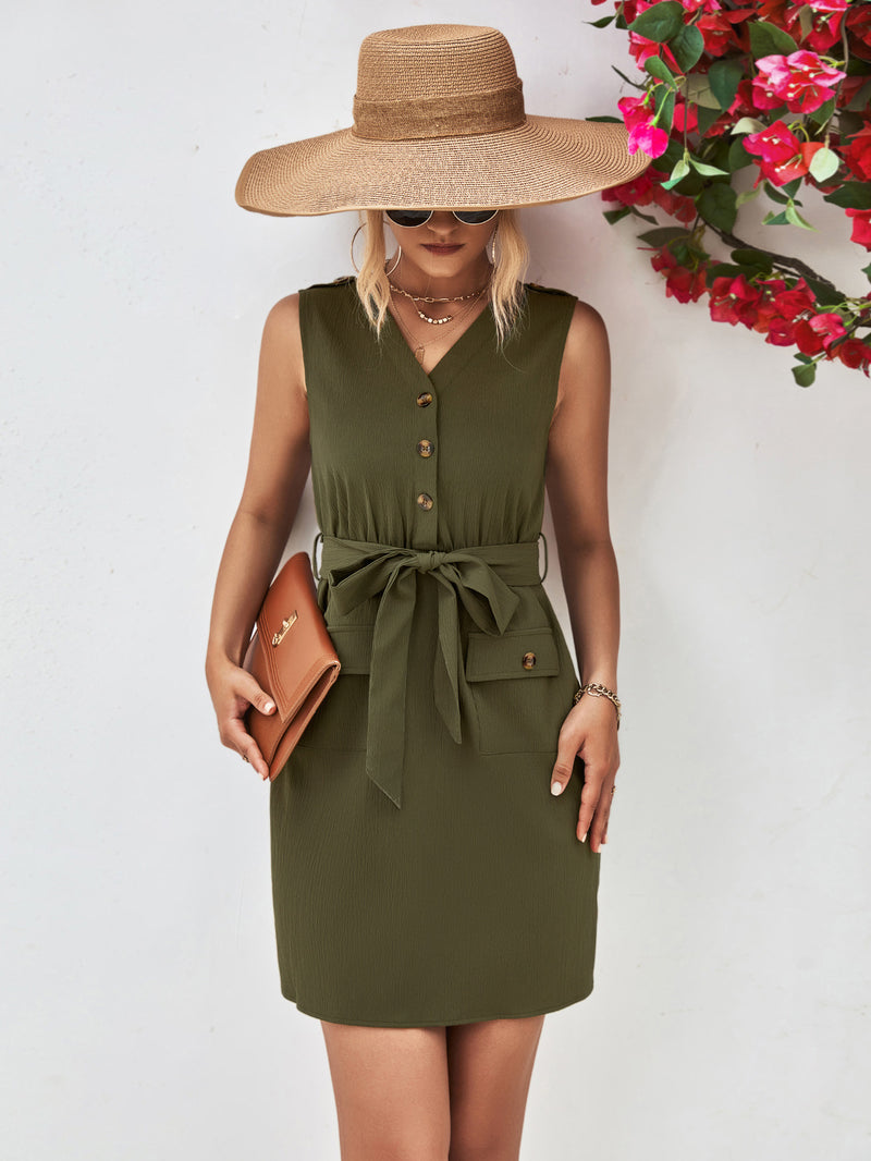 Woman wearing an olive green dress with a wide-brimmed hat and holding a clutch against a white background.