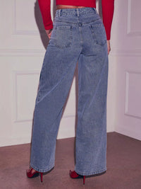 Person wearing blue jeans and a red top against a white wall.