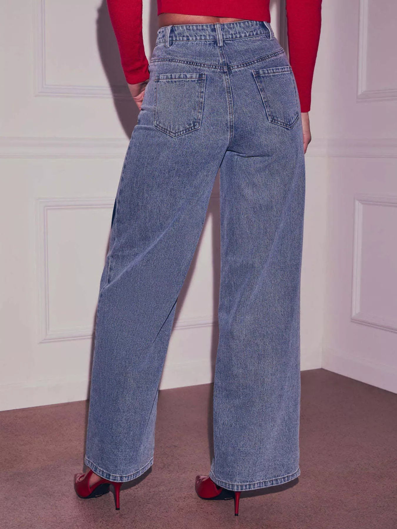 Person wearing blue jeans and a red top against a white wall.
