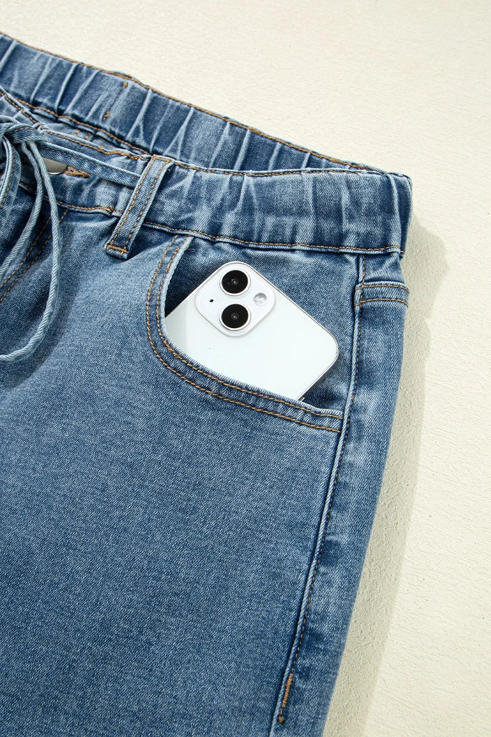 Blue jeans with a white phone in the pocket on a beige background