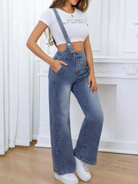 Person wearing a white crop top and blue denim overalls standing in a room with white curtains.