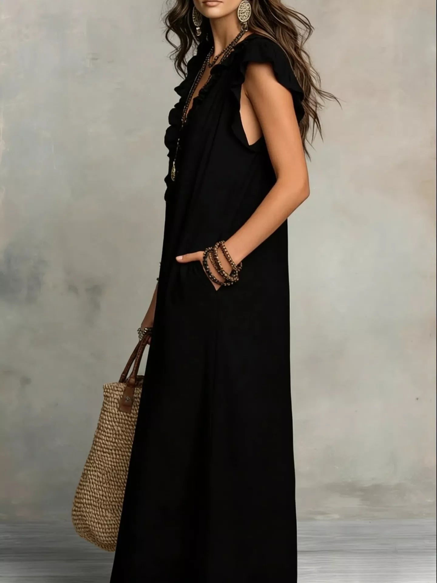 Woman wearing a black sleeveless dress holding a woven handbag against a neutral background