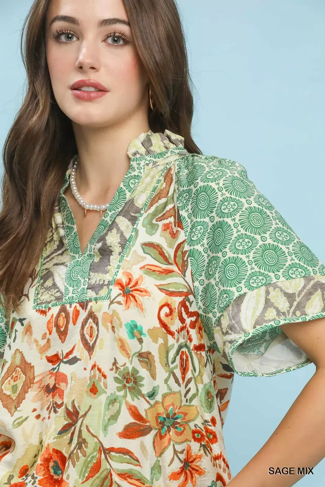 Woman wearing a floral and patterned blouse against a light blue background