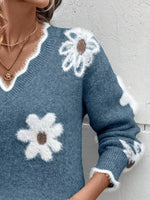 Blue sweater with white flower patterns worn by a person, against a neutral background