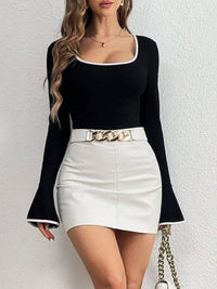 Woman wearing a black top and white skirt with a gold chain belt against a white background