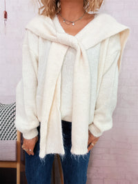 Person wearing a white sweater and scarf with a light background