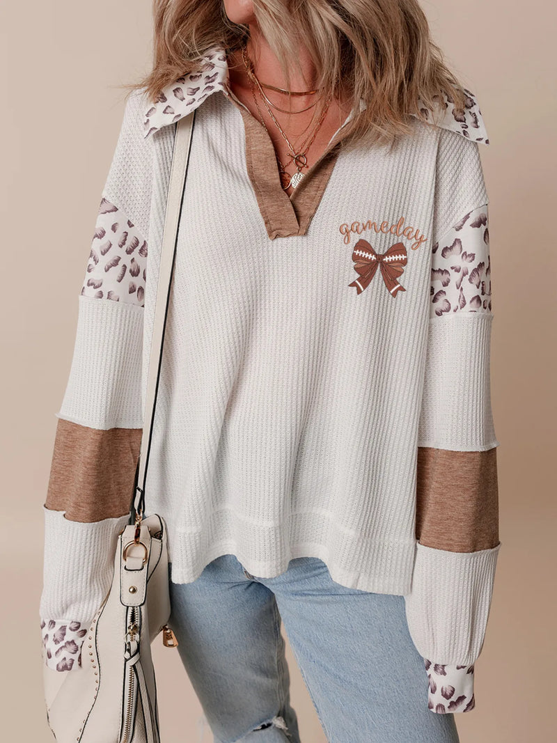 Person wearing a white sweater with leopard print sleeves and a brown bow design, holding a beige handbag.