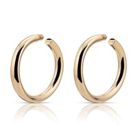 A pair of gold-colored hoop earrings with a sleek, hollow design, crafted from recycled brass with hypoallergenic surgical steel posts.