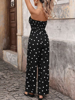 Woman wearing a black polka dot jumpsuit standing on a stone pavement.