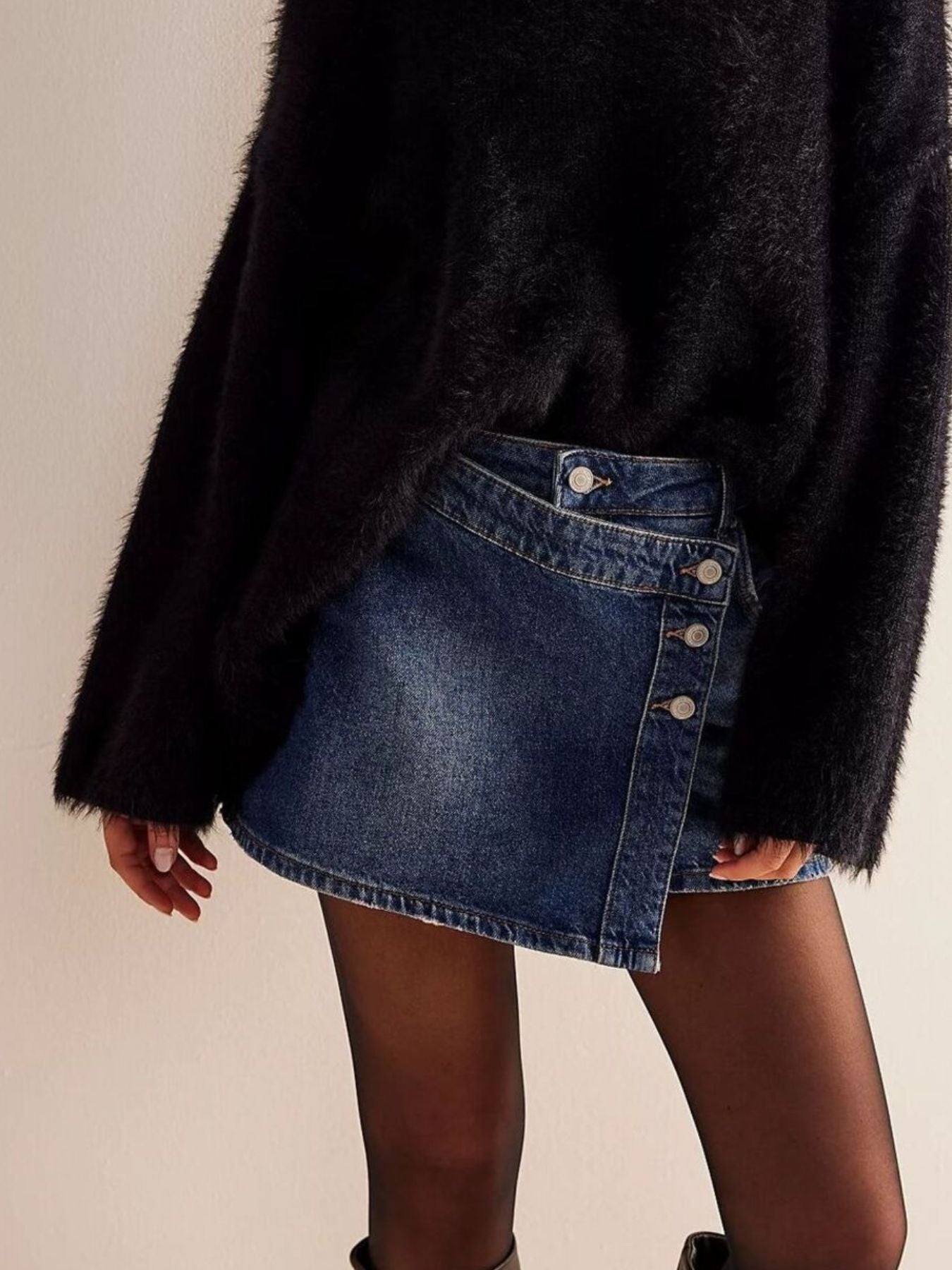 Person wearing a black coat and blue denim skirt on a beige background