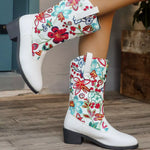White boots with colorful floral patterns worn by a person on a wooden floor.